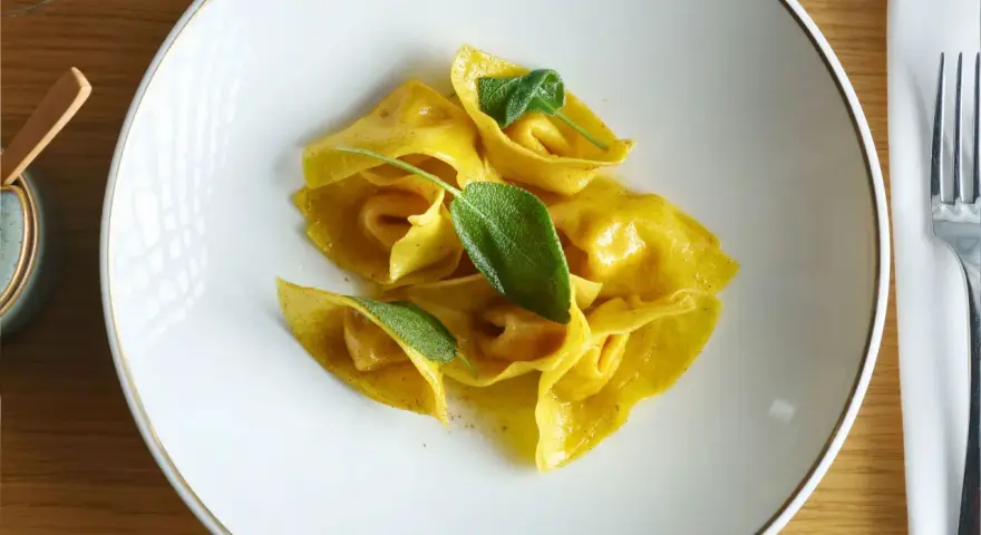 Gelbe Ravioli mit Salbeiblättern auf einem weißen Teller. Ein köstliches Gericht, das zeigt, was ist Ravioli: gefüllte Teigtaschen.