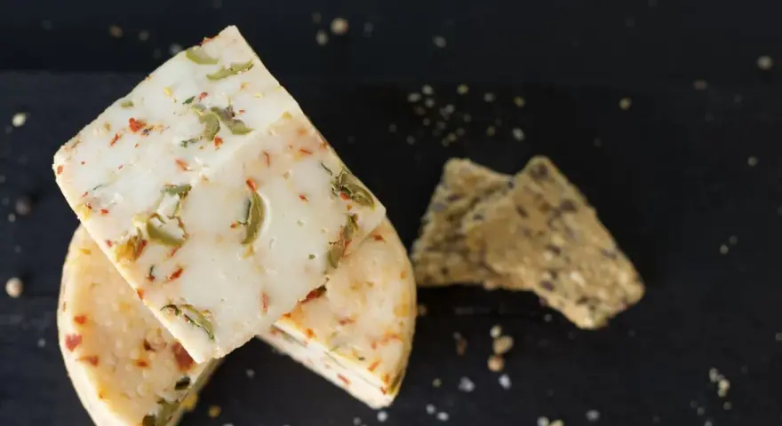 Käse mit Kräutern und Paprika, eine köstliche pecorino alternative, neben knusprigen Crackern auf dunklem Untergrund.