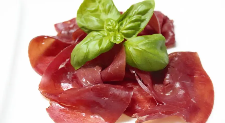 Dünne Scheiben von Bresaola, einem luftgetrockneten Rindfleisch, garniert mit frischem Basilikum.