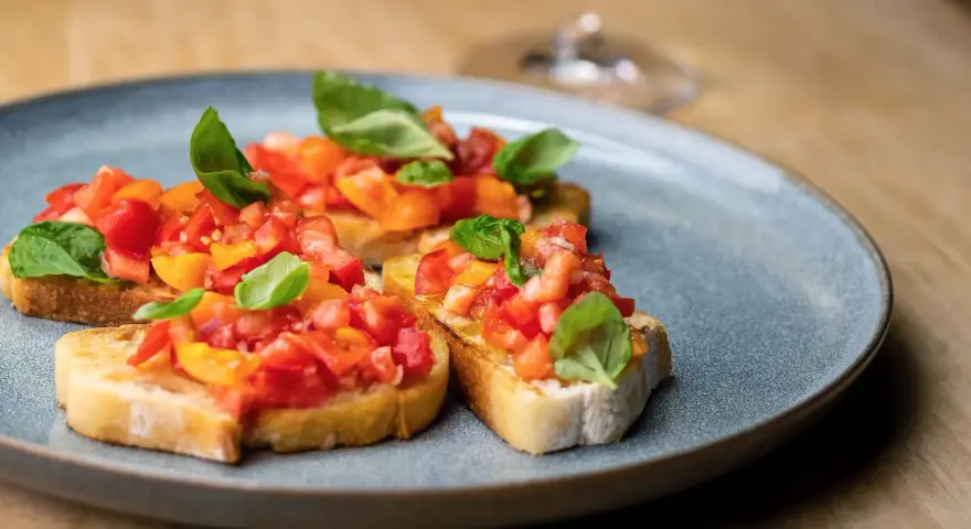 Drei Scheiben geröstetes Brot, belegt mit frischen Tomaten und Basilikum. Ein authentisches rezept bruschetta original italienisch.