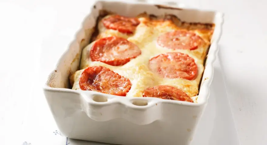 Gorgonzola Lasagne mit Tomaten und geschmolzenem Käse in einer weißen Auflaufform.