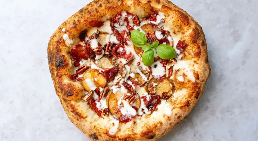Eine köstliche Pizza aus Neapel mit Kartoffelscheiben, Speck, Nüssen und einem Hauch von Basilikum.