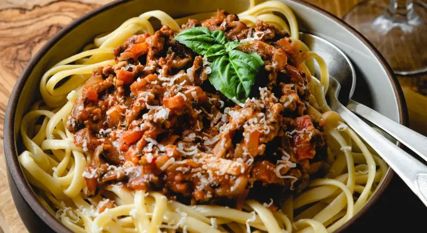 Herzhafte bolognese mit speck, serviert auf Bandnudeln, garniert mit Basilikum und Parmesan.