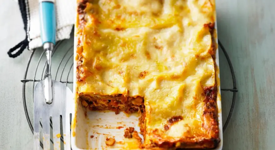 Eine goldbraun überbackene Lasagne mit einer cremigen Käseschicht. Ein Stück ist bereits entnommen, was die saftige Füllung offenbart. Diese Pistazien Lasagne sieht köstlich aus!