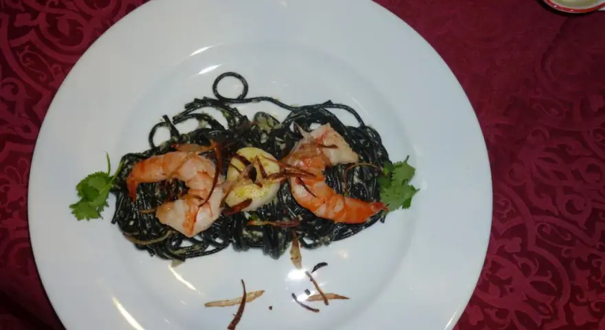 Schwarze Spaghetti mit Garnelen, garniert mit Koriander und knusprigen Zwiebeln. Ein köstliches Gericht, das auf einem weißen Teller serviert wird.