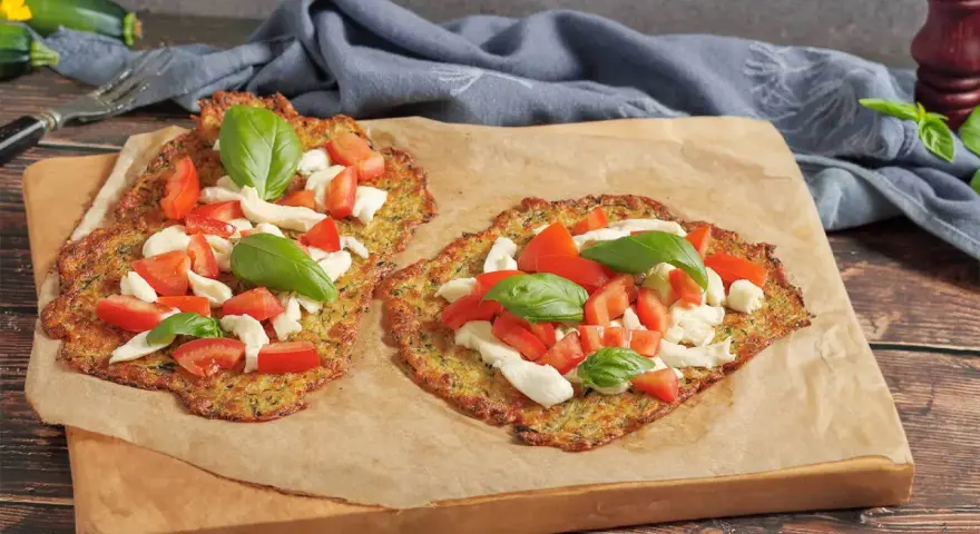 Zwei leckere Zucchini-Pizzen mit Mozzarella, Tomaten und Basilikum auf Backpapier.
