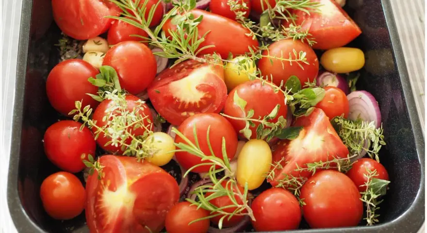Tomaten einkochen im Backofen: Frische Tomaten, Zwiebeln und Kräuter in einer Auflaufform, bereit für den Ofen.