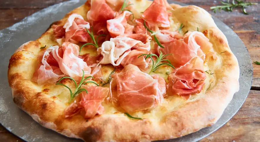 Eine köstliche biancaneve pizza mit zartem Schinken und Rosmarin, auf einem Pizzastein serviert.
