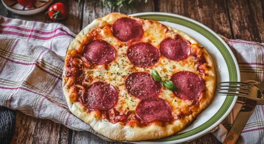 Eine köstliche Pizza Salami mit geschmolzenem Käse und frischem Basilikum auf einem rustikalen Holztisch.