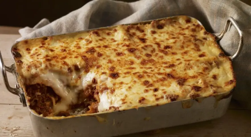 Herzhafte Lasagne mit goldbraun überbackener Käseschicht und einem Hauch von Creme Fraiche, serviert in einer Metallform auf Holztisch.
