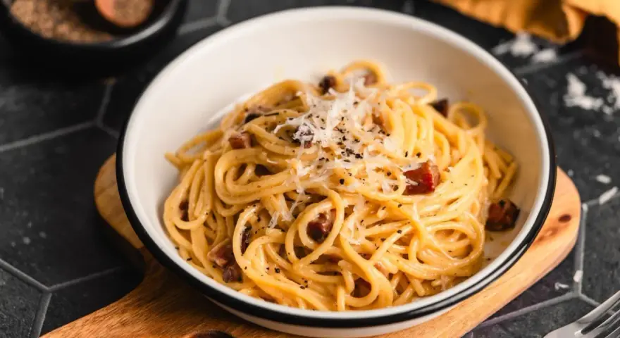 Eine Schüssel cremiger Pasta Carbonara, garniert mit frisch geriebenem Parmesan und schwarzem Pfeffer, bereit zum Genießen.