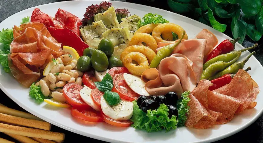Eine üppige antipasti platte mit Schinken, Salami, Oliven, Artischocken, Tomaten-Mozzarella-Salat und frittierten Ringen.