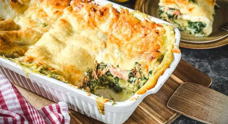 Eine köstliche, goldbraun überbackene italienische Lachslasagne mit Spinat und cremiger Sauce. Ein Stück ist bereits serviert.