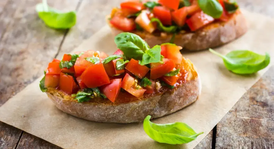 Zwei Bruschetta mit frischen Tomaten und Basilikum, garniert mit einem Hauch von Paprika, auf rustikalem Holz.