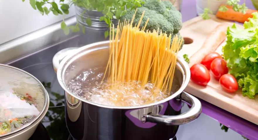 Spaghetti kochen in sprudelndem Wasser. Die richtige **Tagliatelle Kochzeit** ist entscheidend für ein perfektes Pastagericht. Frisches Gemüse wie Brokkoli, Karotten und Tomaten liegen bereit.