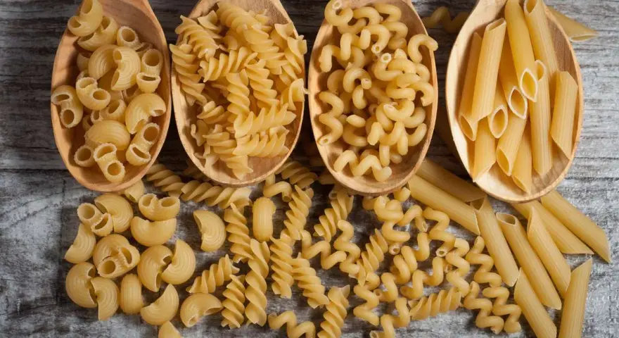 Vier Holzlöffel mit verschiedenen Nudelsorten: Maccheroni, Fusilli, Cavatappi und Penne. Die perfekte Menge Nudeln pro Person für ein köstliches Essen.