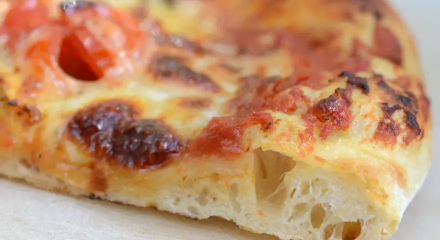 Ein Stück Pizza mit geschmolzenem Käse und Tomaten. Der Teig ist luftig und goldbraun gebacken, typisch für eine Pizza Sourdough.