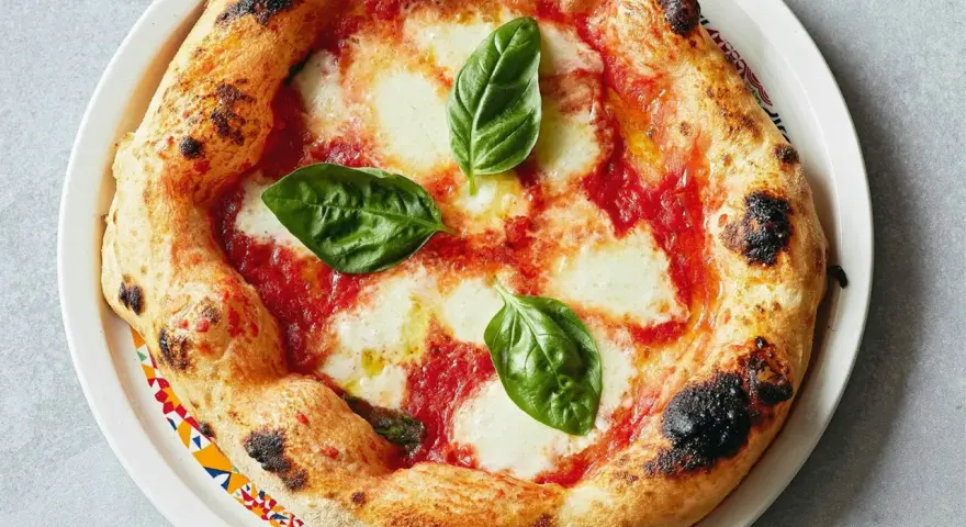 Eine original Pizza Margherita mit geschmolzenem Mozzarella, Tomatensauce und frischem Basilikum. Der Rand ist goldbraun und leicht angekohlt.