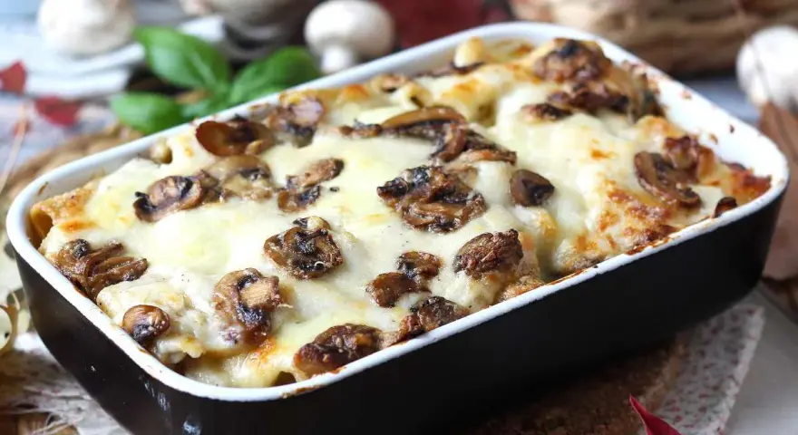 Herzhafte Lasagne al funghi mit geschmolzenem Käse und Pilzen, serviert in einer Auflaufform.