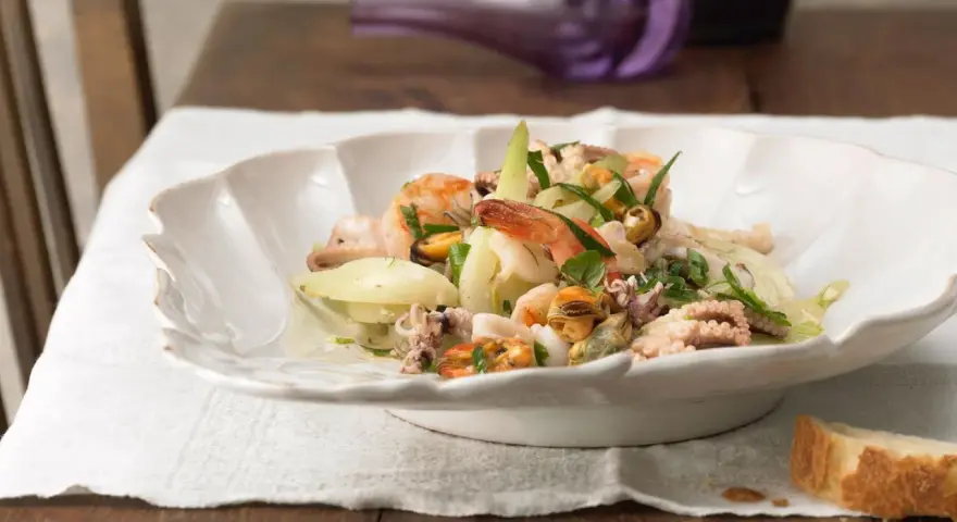 Frischer insalata di mare mit Garnelen, Muscheln und Tintenfischringen, garniert mit Kräutern und Zwiebelringen.