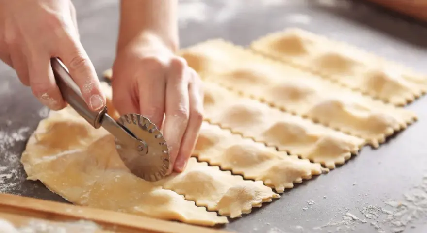 Hände schneiden mit einem Teigrädchen frische Ravioli. Das sind die besten Ravioli Rezepte zum Nachmachen.