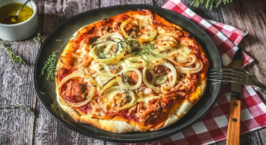Italienisches Thunfisch Pizza Rezept: Eine köstliche Pizza mit Thunfisch, Zwiebeln und Käse, serviert auf einem Holztisch.