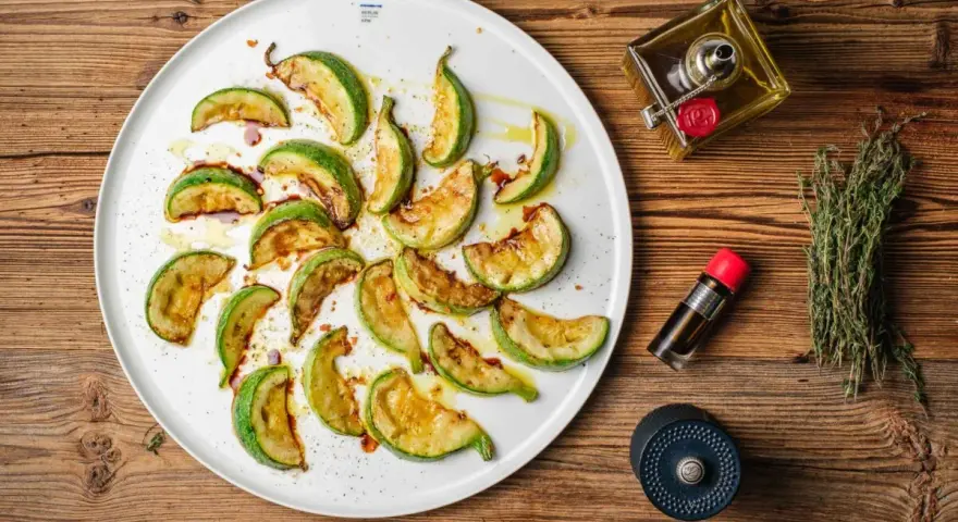 Gebratene Zucchinischeiben auf einem Teller, beträufelt mit Öl und Balsamico. Ein köstlicher Zucchini-Salat, bereit zum Genießen.