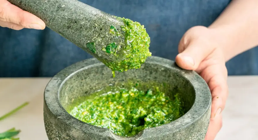 Frische Kräuter werden im Mörser zermahlen, um zu zeigen, wie man Pesto zubereitet.