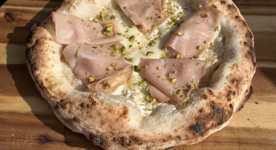 Pizza mit Mortadella und Pistazien auf luftigem pizzateig mit hefe. Der Rand ist knusprig und leicht verbrannt.