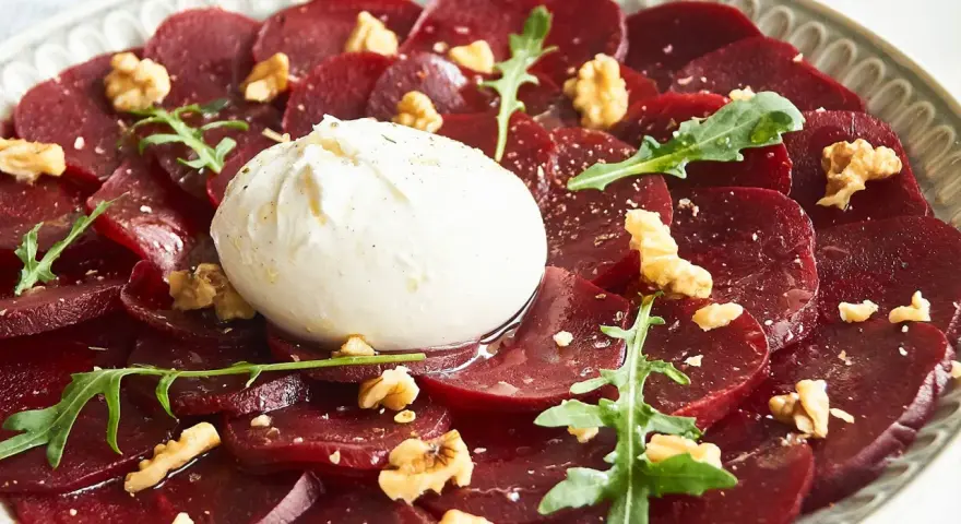 Rote Bete Carpaccio mit Burrata, Walnüssen und Rucola. Ein köstlicher Salat, der auf einem Teller serviert wird.