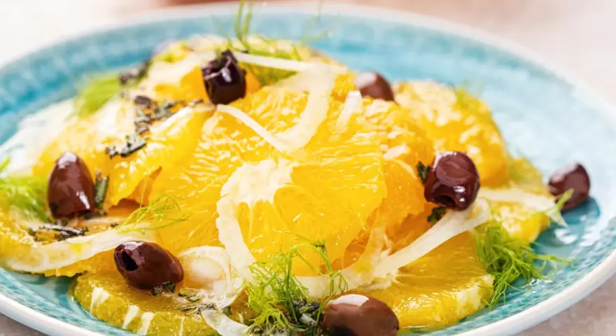 Erfrischender orangensalat sizilianisch mit Fenchel und dunklen Oliven auf einem blauen Teller.