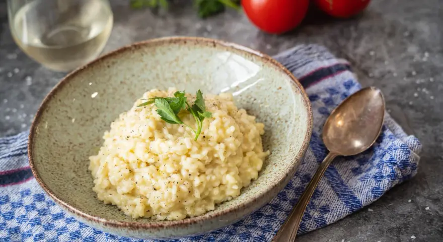 Cremiges Risotto, perfekt als Grundrezept für viele Variationen. Mit frischer Petersilie garniert, daneben ein Glas Weißwein und Tomaten.