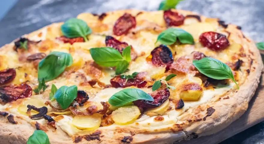 Leckeres Pizza Bianca Rezept mit Kartoffelscheiben, getrockneten Tomaten und frischem Basilikum.
