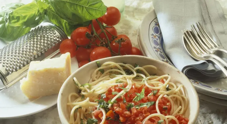 Spaghetti mit frischen Kräutern und gehackten Tomaten aus der Dose. Dazu ein Stück Parmesan, frische Tomaten und ein Grater. Perfekt für einfache Rezepte mit gehackten Tomaten aus der Dose.
