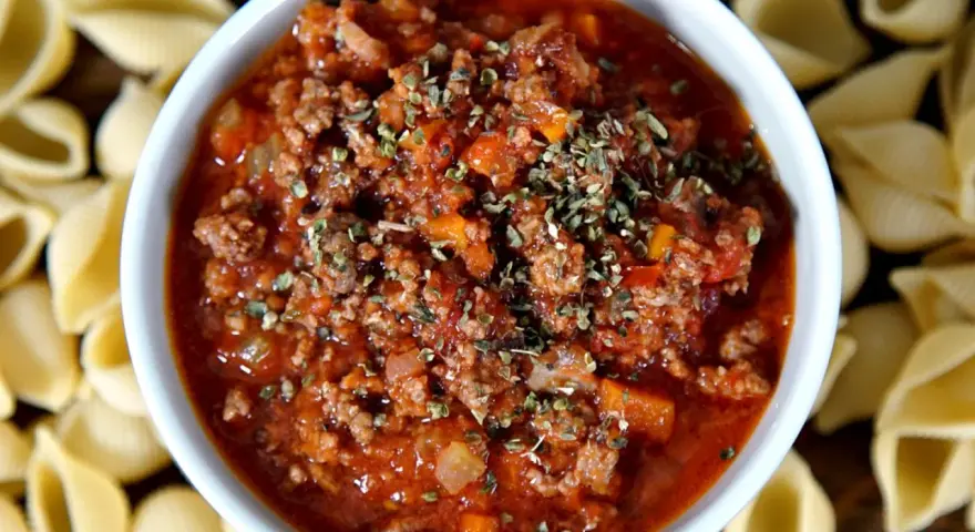 Herzhafte pancetta bolognese in einer Schüssel, umgeben von ungekochten Muschelnudeln.