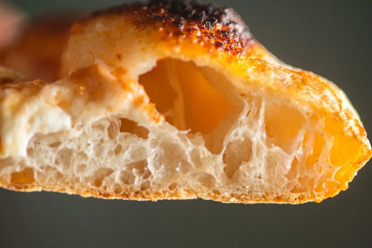 Nahaufnahme eines luftigen pizzateigs, der 24 Stunden gereift ist. Die Kruste ist goldbraun und leicht angekohlt, das Innere zeigt gro&szlig;e Blasen.