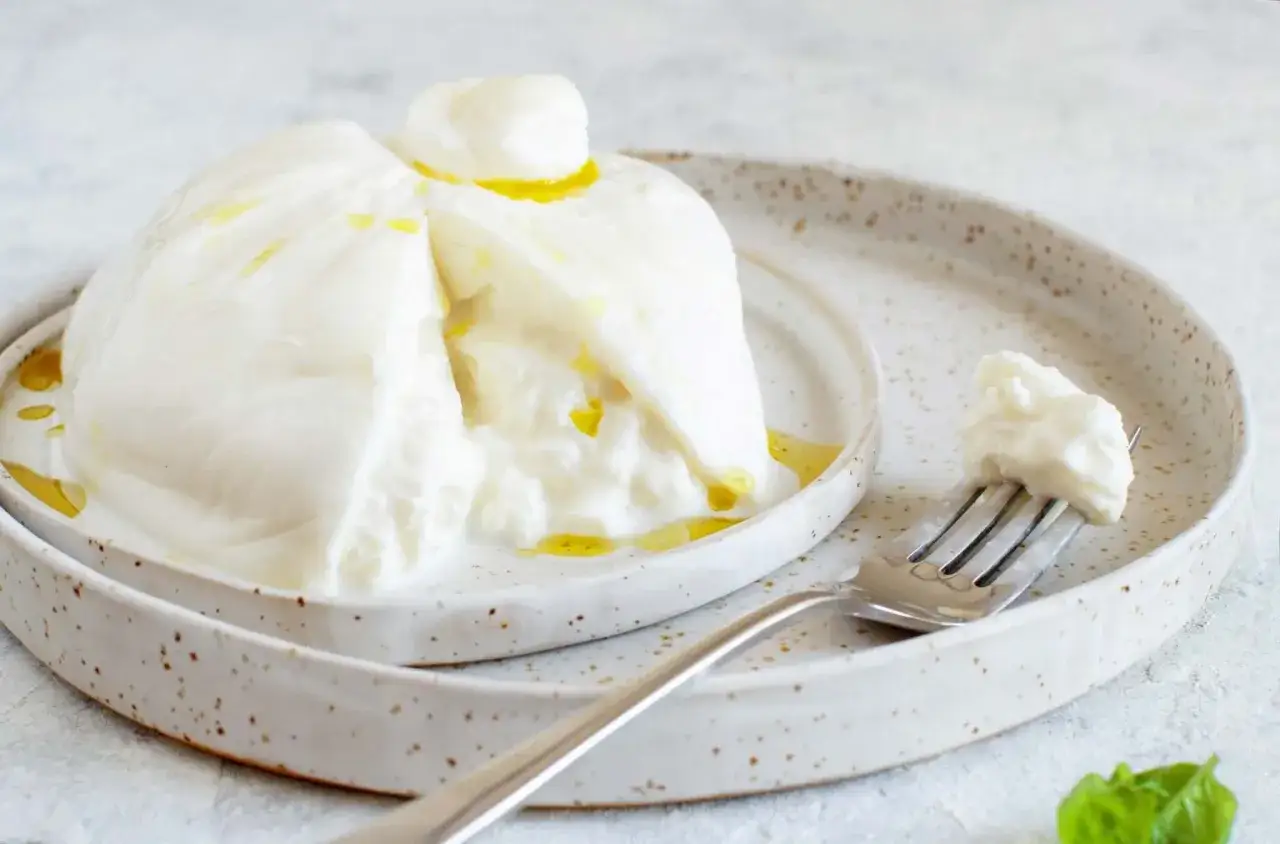 Ein frischer Burrata mit cremigem, weichem Kern, betr&auml;ufelt mit Oliven&ouml;l. Ein Gabelst&uuml;ck zeigt die k&ouml;stliche Textur.