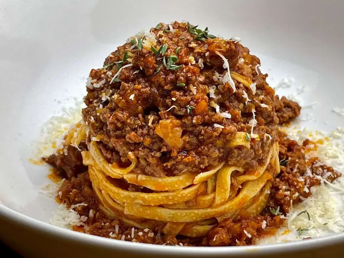 Ein Turm aus Tagliatelle, bedeckt mit einem herzhaften Sos Bolognese und bestreut mit Parmesan und Kr&auml;utern.