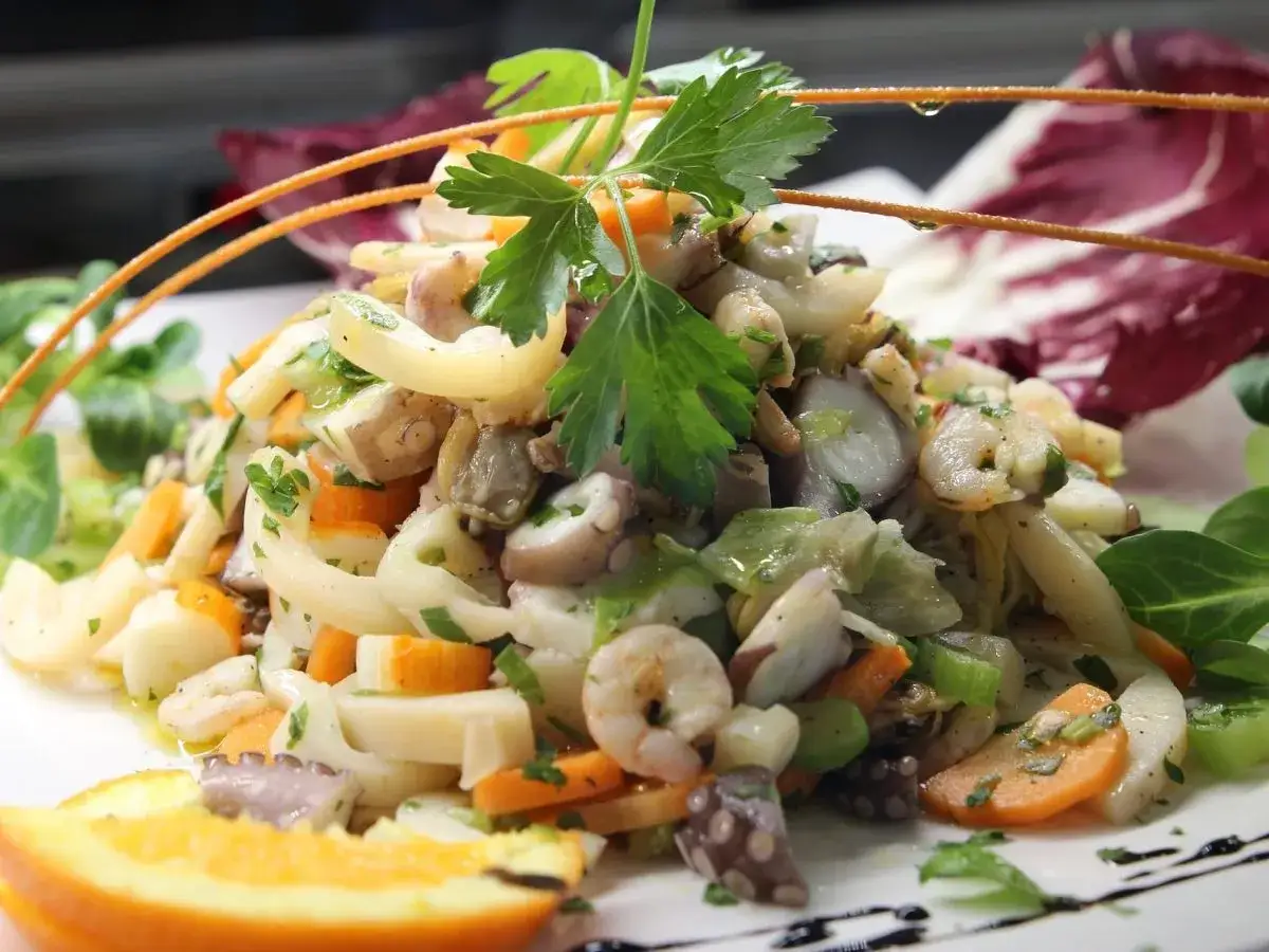 Frischer insalata di mare mit Oktopus, Garnelen, Karotten und Kr&auml;utern, garniert mit Orangenspalte und Radicchio.