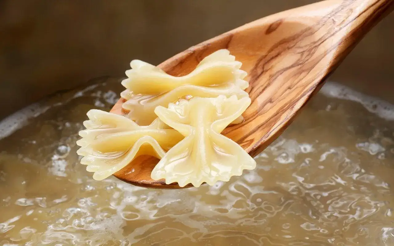 Holzkochlöffel mit Farfalle-Nudeln über kochendem Wasser. Die perfekte Farfalle Kochzeit ist fast erreicht.