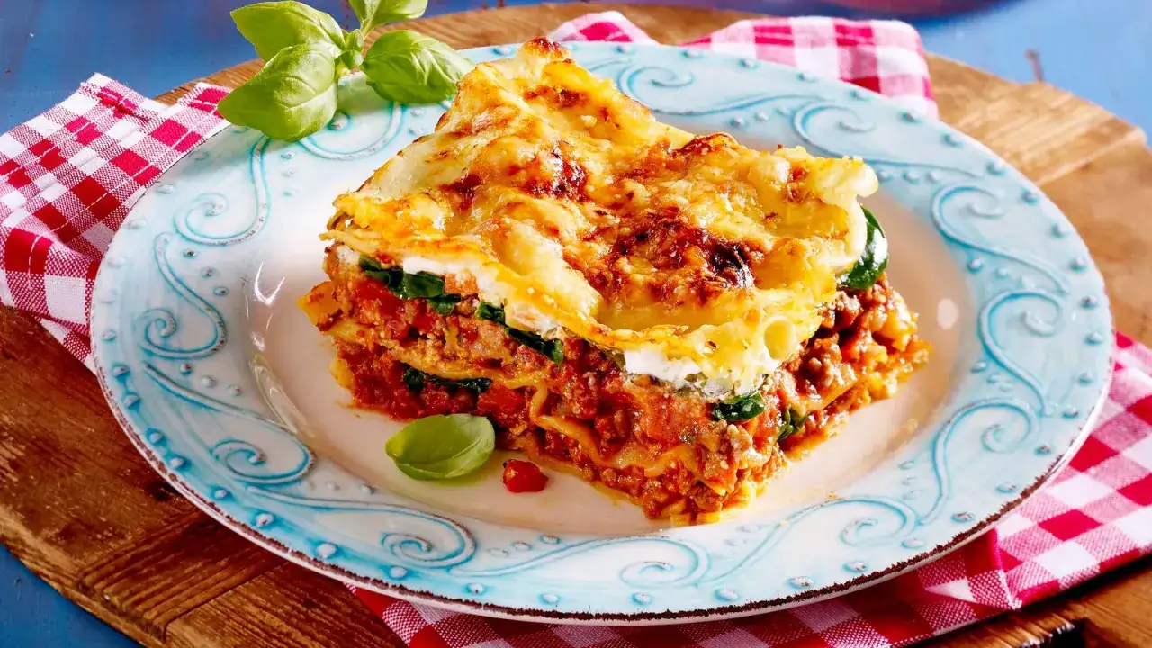 Ein St&uuml;ck Lasagne mit Hackfleischsauce und Spinat, &uuml;berbacken mit K&auml;se und einem Klecks Creme Fraiche. Garniert mit Basilikum.