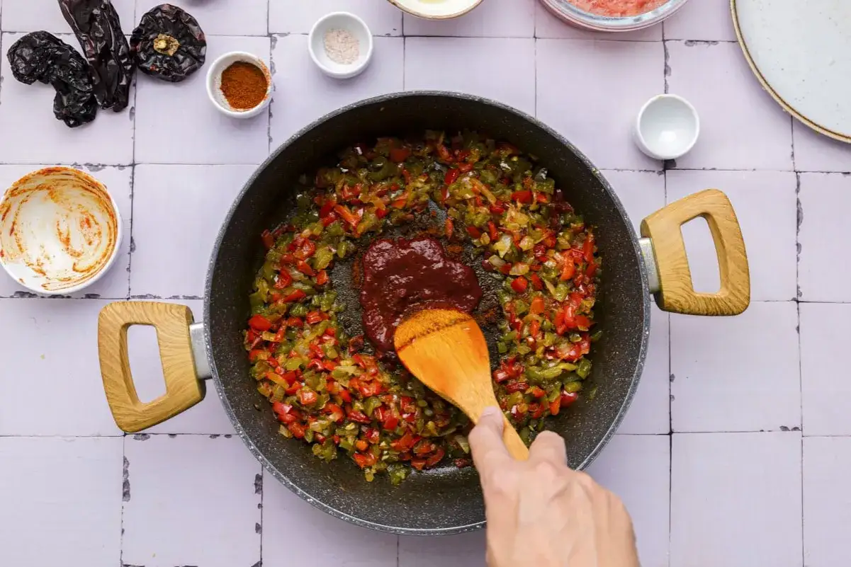 Sofrito, eine Mischung aus gebratenem Gem&uuml;se, wird in einer Pfanne mit einer L&ouml;ffelspachtel vermischt.