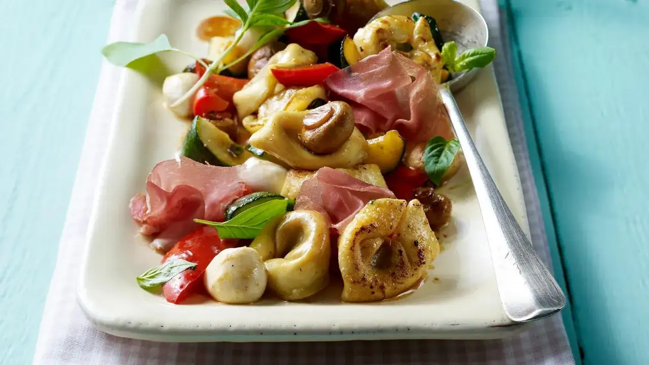 Ein köstlicher Tortellini-Salat mit Rucola, Mozzarella, Tomaten, Zucchini und Schinken.