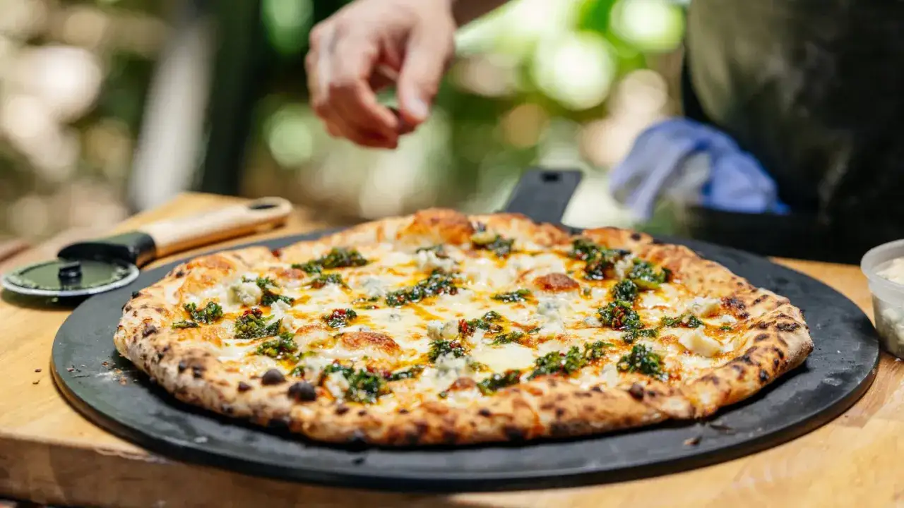 Eine k&ouml;stliche Quattro Formaggi Pizza mit geschmolzenem K&auml;se und gr&uuml;nen Kr&auml;utern, bereit zum Anschneiden.
