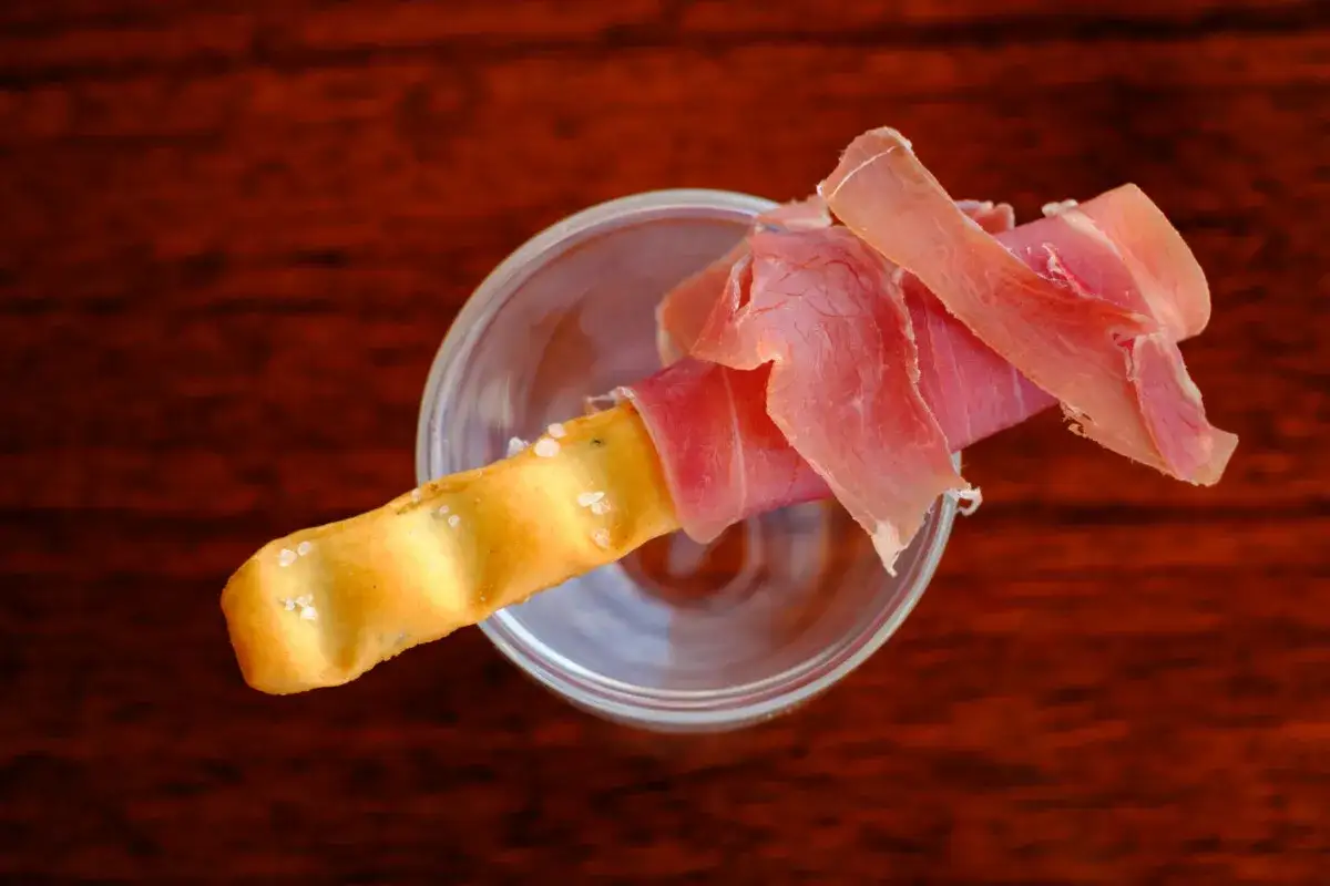 Ein knuspriger Grissini, umwickelt mit zartem Schinken, ruht in einem Glas.