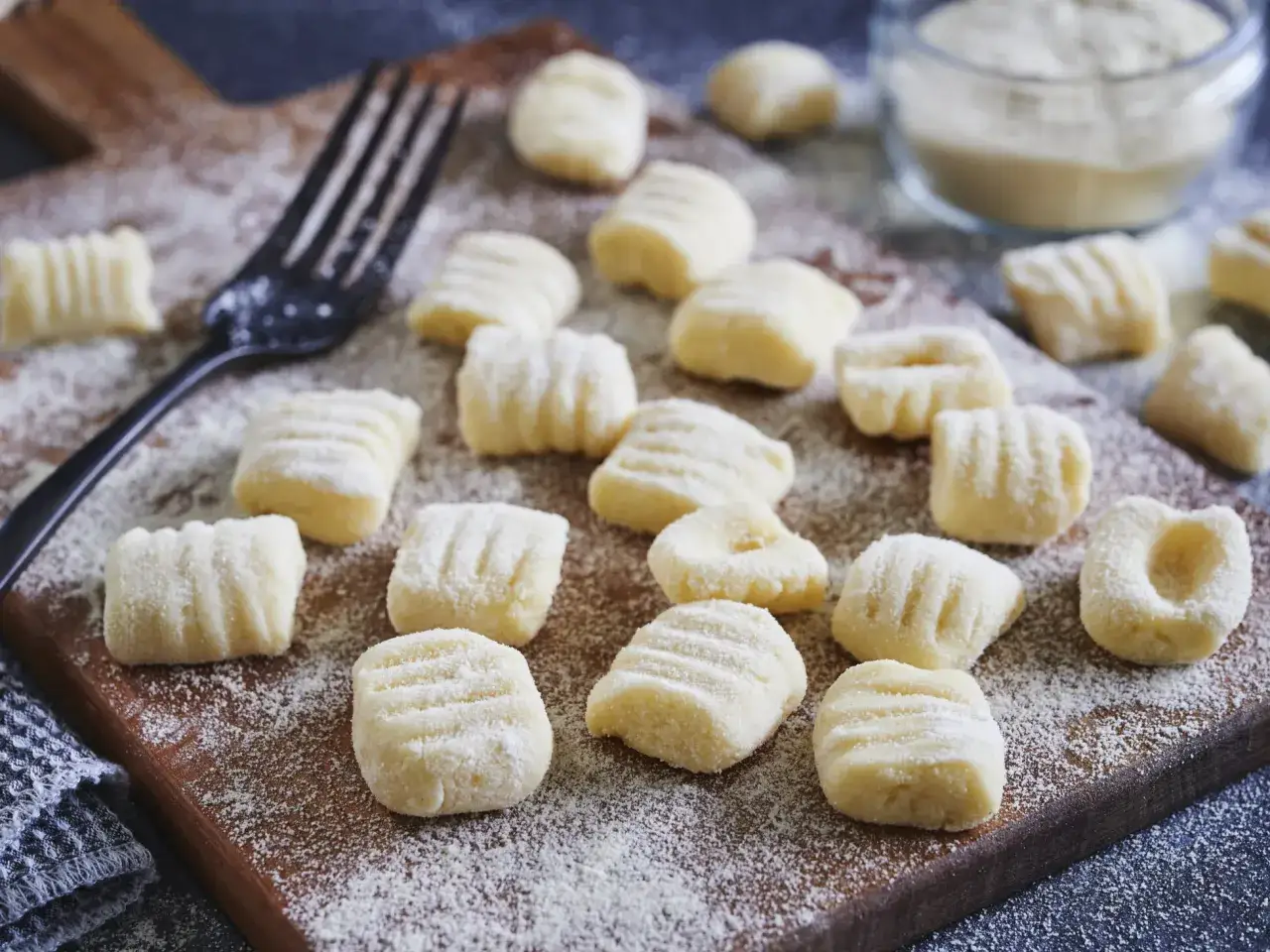Frische Gnocchi, bereit für italienische Rezepte, liegen auf einem Holzbrett, bestäubt mit Mehl. Eine Gabel liegt daneben.