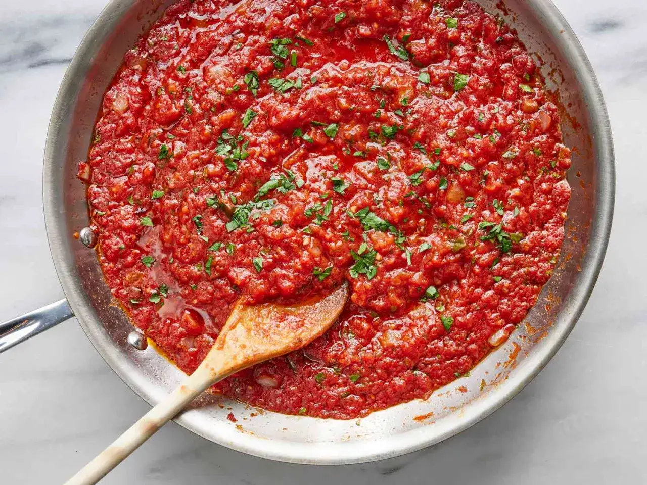 Eine Pfanne mit köstlicher, hausgemachter marinara sauce, garniert mit frischer Petersilie. Ein Holzlöffel rührt in der sämigen Sauce.