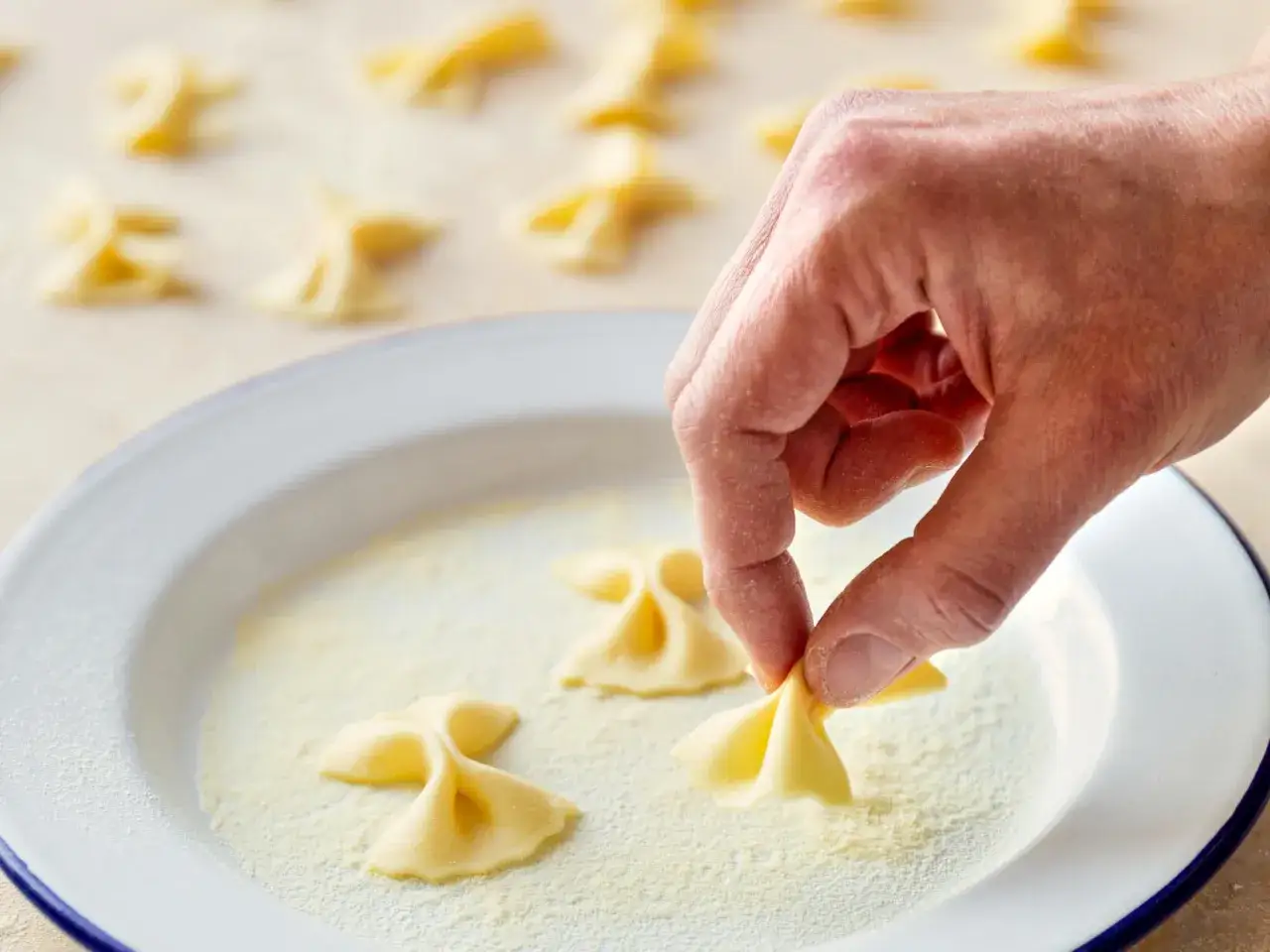 Hand formt frische Farfalle-Nudeln in einer Schüssel mit Mehl.