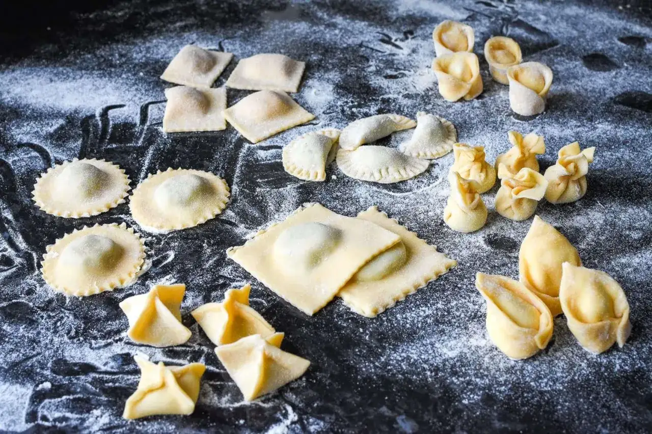 Frische Ravioli in verschiedenen Formen, von quadratisch bis rund, liegen auf einer bemehlten Fläche. Was ist Ravioli? Gefüllte Teigtaschen, bereit zum Kochen.