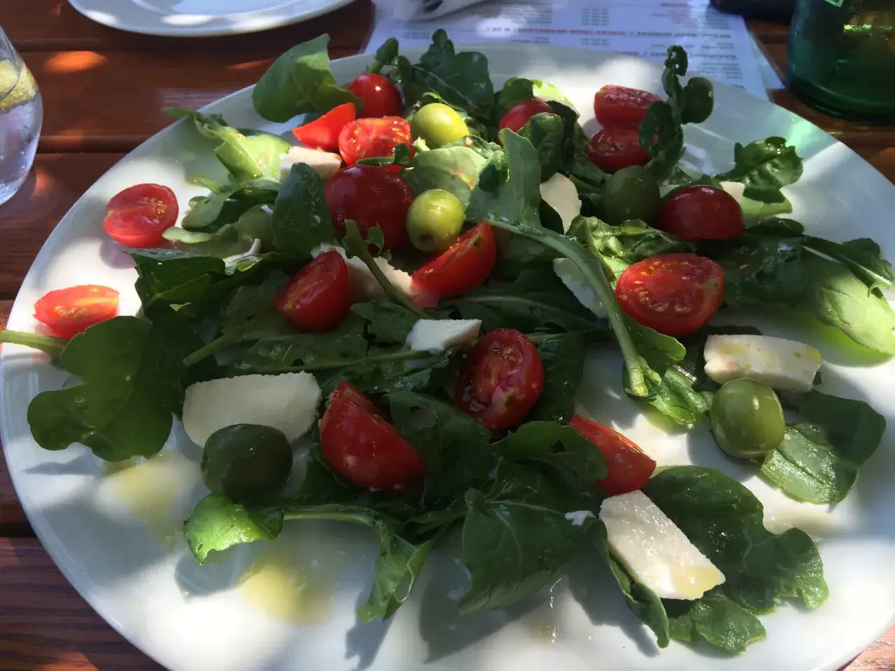 Frischer Rucola Salat mit Kirschtomaten, Mozzarella und gr&uuml;nen Oliven, betr&auml;ufelt mit Oliven&ouml;l.